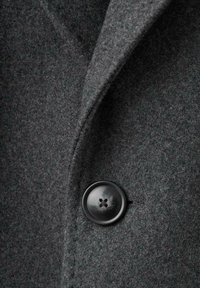 Tessuto di cappotto di lana grigia con una texture liscia, caratterizzato da un bottone nero arrotondato con quattro fori e un design con colletto a scollatura.