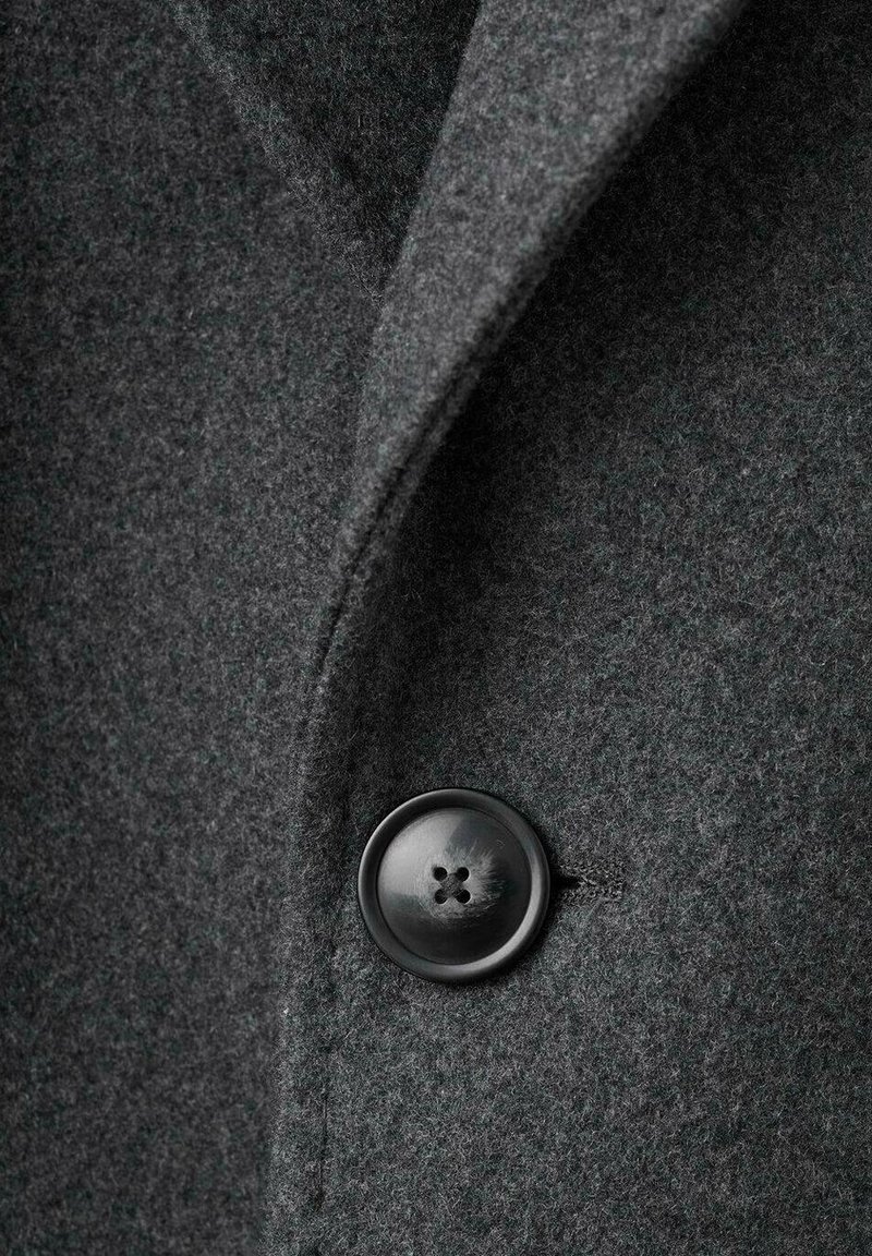 Grå ullrocktyg med en jämn textur, med en rund svart knapp med fyra hål och en design med notched krage.
