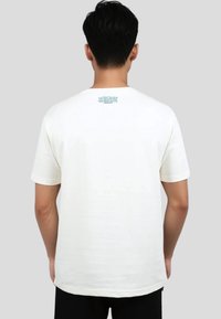 Camiseta de algodón color crema con mangas cortas y escote redondeado. Presenta un gráfico azul en la parte superior de la espalda. Textura suave.