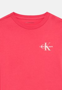 Różowa bawełniana koszulka z okrągłym dekoltem, z białym logo „Calvin Klein Jeans” na lewej stronie klatki piersiowej. Gładka faktura, casualowy styl.