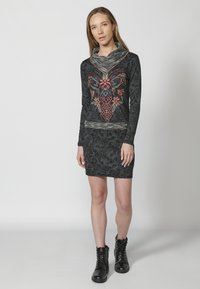 Schwarzes langärmliges Kleid mit kunstvollen Blumenstickereien in Rot und Blau, mit einem Schalkragen und einer figurbetonten Silhouette bis über das Knie.