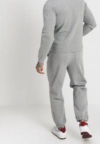 Grå sweatshirt och byxor i mjukt bomullsblandning, med elastiska manschetter och en avslappnad passform. Sneakers i röd och vit.