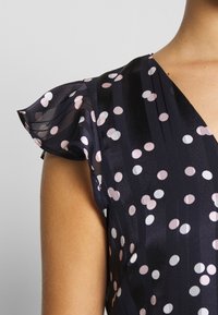 Navy dress with sheer, ruffled sleeves, featuring a polka dot pattern in pink and white on a subtle striped background.