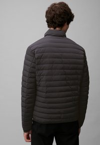 Giacca trapuntata grigia scura con cuciture orizzontali, colletto alto e texture liscia. Presenta polsini elasticizzati e una vestibilità comoda.