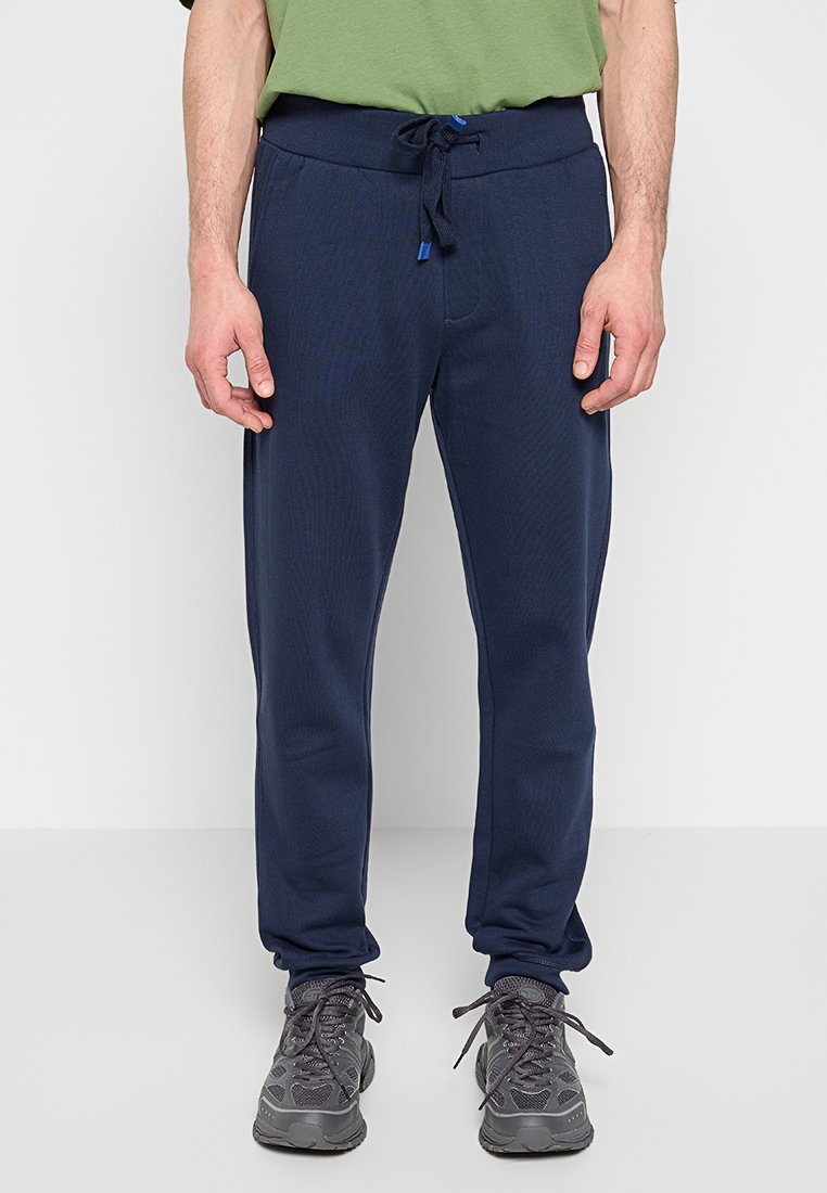 Pantaloni tuta blu navy con finitura texurizzata, vita elastica con cordino blu e gambe affusolate. Indossati con scarpe sportive grigie.