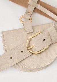 Bež torbica od kože s uzorkom krokodila, s kopčom u zlatnoj boji i podešivim remenom. Ima zaobljen oblik i glatku teksturu.