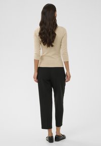 Haut beige à manches longues avec une coupe ajustée, associé à un pantalon noir fuselé et des chaussures noires brillantes, vu de dos.