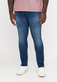 Mörkblå slim-fit jeans i denim, med en urtvättad finish. Kombineras med vita sneakers och en ljusgrå T-shirt.