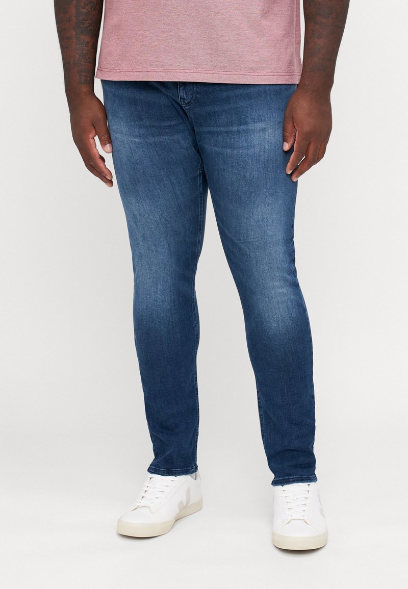 Mörkblå slim-fit jeans i denim, med en urtvättad finish. Kombineras med vita sneakers och en ljusgrå T-shirt.