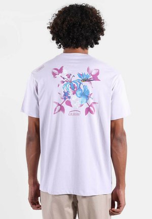 T-shirt en coton violet clair avec un motif floral bleu et rose au dos. Coupe décontractée avec col rond et manches courtes.