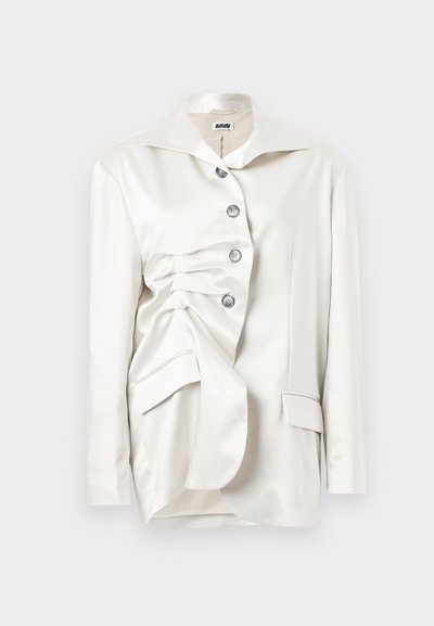 Blazer bianco in satin con un design strutturato, caratterizzato da chiusura a bottoni, colletto oversize e dettaglio di tessuto drappeggiato su un lato.
