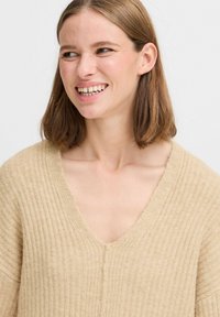 Hellbeige gestreifter Pullover mit tiefem V-Ausschnitt und überschnittenen Schultern, aus einem weichen, strukturierten Material gefertigt.
