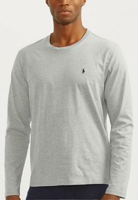 Γκρι βαμβακερή μπλούζα με μακριά μανίκια, στρογγυλή λαιμόκοψη και μικρό κεντημένο λογότυπο στο στήθος. Απαλή υφή, κανονική εφαρμογή.