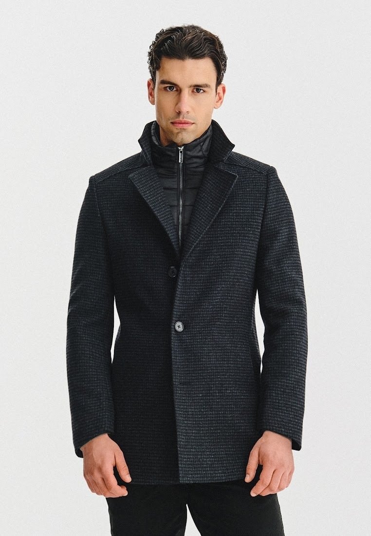 Czarny, teksturowany płaszcz z wyłogami, z zapięciem na jeden guzik oraz przymocowaną, zapinaną na zamek warstwą ocieplającą pod spodem.