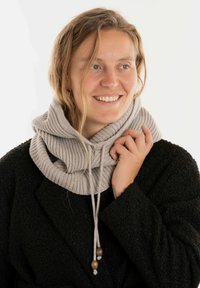 Grijze geribbelde sjaal met kraag en trekkoorden, versierd met houten accenten, gedragen over een zwarte fuzzy jas. Zachte textuur en gelaagd ontwerp.