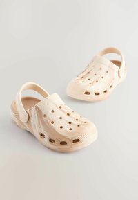 Beige träskor med en texturerad yta, öppen tå-design och flera ventilationshål. Har en bakrem för säker passform.