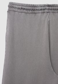 Grau Sweatpants aus glattem Stoff. Mit elastischem Bund und Seitentasche. Schlichtes, ungeschmücktes Design ohne Muster oder Akzente.
