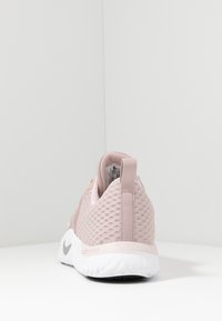 Rosa sportskor med övre i mesh, gummisula och vadderad krage. Har en dragflik vid hälen och en liten grå logotyp på sidan.