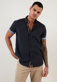 Cămașă marină cu mânecă scurtă, cu manșete din denim, design cu butoane, detaliu discret în dungi la guler și material ușor.