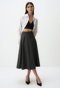 Zwarte crop top met wikkels, witte shirt met knopen en een grijze flared midi rok met een gladde textuur. Zwarte puntige hakken maken de outfit compleet.