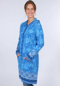 Blau gemusterte Kapuzenstrickjacke mit Knöpfen, Seitentaschen und dekorativen Bündchen, die mit feinen weißen und marineblauen Akzenten verziert sind.