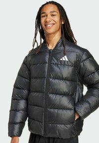 Nuori mies, jolla on pitkät dreadsit, hymyilee mustassa toppatakin kanssa, jossa on vetoketju ja Adidas-logo vasemmassa rinnassa.