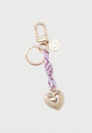 Goudkleurige sleutelhanger met karabijnhaak, ronde en "G" logo bedels, en een geknoopte paarse stof die een hartvormige hanger vasthoudt waarop "GUESS" is gegraveerd.