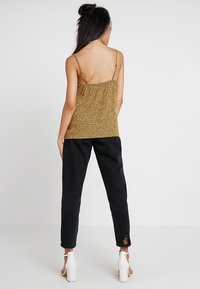 Gul leopardmönstrad tanktop med tunna band, kombinerad med svarta, avsmalnande jeans med slitna detaljer vid vristen och vita klackar.