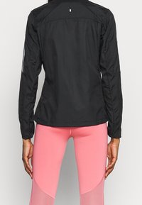 Chaqueta atlética negra con un diseño elegante, que presenta mangas largas, un dobladillo redondeado y franjas reflectantes en los brazos.