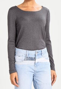 Gray long-sleeve top with a wide crew neckline, paired with light blue denim jeans featuring a mixed media waistband and varied textures.