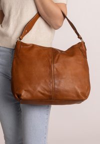 Borsa a spalla in pelle marrone con una forma morbida e floscia. Presenta una singola tracolla ampia e dettagli di cucitura sottili. Adatta per uso quotidiano.