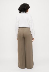 Bijela košulja dugih rukava, u kombinaciji s širokim hlačama visokog struka u bež boji, s glatkom teksturom i elastičnom waistband.