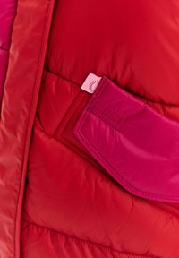 Detailní záběr na složenou červenou a růžovou polstrovanou tkaninu se šitými okraji a malou nálepkou s ikonou slunce.