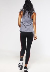 Top grigio senza maniche abbinato a leggings neri con strisce laterali rosse e scarpe da ginnastica nere. Tessuto liscio e design aderente.