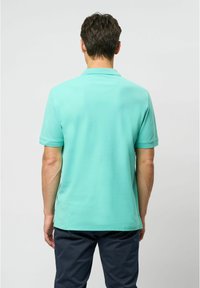 Turkos polotröja med korta ärmar, texturerad tyg och en diskret krage. Bärs med navybyxor, vilket visar en enkel design.