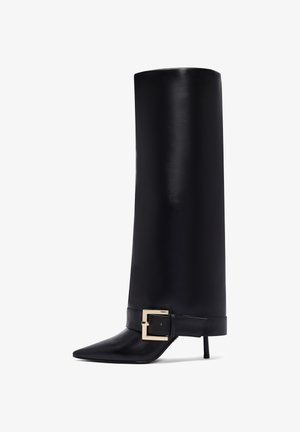 Botte en cuir noir montante à bout pointu et tige large. Elle présente un accent de boucle carrée dorée sur la lanière de la cheville et un talon stilettos.