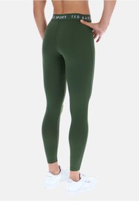 Olive zelené legíny s priliehavým dizajnom, obsahujúce vysoký pás označený "TED BAKER SPORT" a hladkú, elastickú látku.
