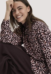 Rosa Bluse mit einem schwarz-braunen Leopardenmuster, mit einem Kordelzug-Halsauschnitt und lockeren, langen Ärmeln. Dunkelbrauner Stoff an der Unterseite.