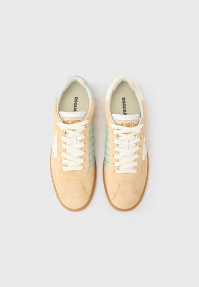 Μπεζ σουέντ αθλητικά παπούτσια με ταιρκουάζ λεπτομέρειες και λευκά κορδόνια. Διαθέτουν λαστιχένια σόλα και λεπτά, υφή μοτίβα στο πλάι. Η επωνυμία είναι εμφανής στη γλώσσα.