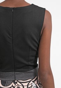 Haut noir sans manches avec une texture lisse et une fermeture éclair discrète ; comprend une ceinture grise au-dessus d'une jupe à motifs.