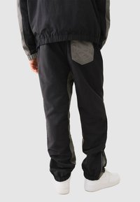 Schwarze Herren-Cargohosen mit grauen Akzenten, elastischen Knöchellöchern und seitlichen Reißverschlüssen. Mit einer aufgesetzten Tasche und einer strukturierten Oberfläche.