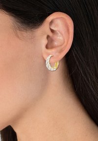 Guld- och vita hoopörhängen med en vriden design. Slät metallisk yta med växlande spiralmönster. Passar både för avslappnad och formell klädsel.