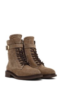 Bottes en suede marron à lacets avec une fermeture éclair sur le côté, un col rembourré et un accent en boucle métallique. Semelle épaisse et bout rond pour plus de stabilité.