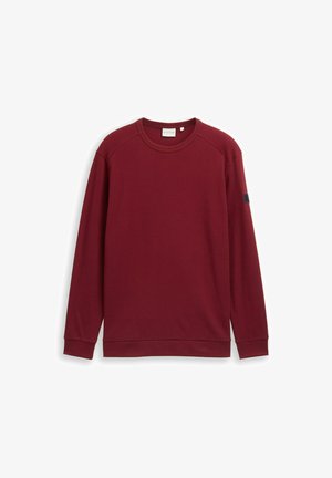 Burgundska dolgimi rokavi majica s teksturo rebraste, okroglim ovratnikom in majhnim temno akcentnim znakom na levi rami.