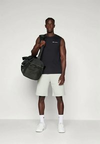 Čierne tielko bez rukávov, svetlošedé šortky, drží čiernu športovú tašku. Biely tenisky a ponožky. Jednoduchý dizajn s logom značky na tričku.