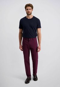 Marine crew-neck t-shirt gecombineerd met maroon slim-fit broeken. Textuurstof en knoopsluiting op de broeken, gedragen met donkerbruine instappers.