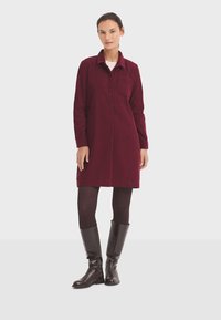 Vestido camisero de pana burdeos con cuello, botones frontales y bolsillo lateral. Llevado con leggings negros y botas altas de cuero marrón.