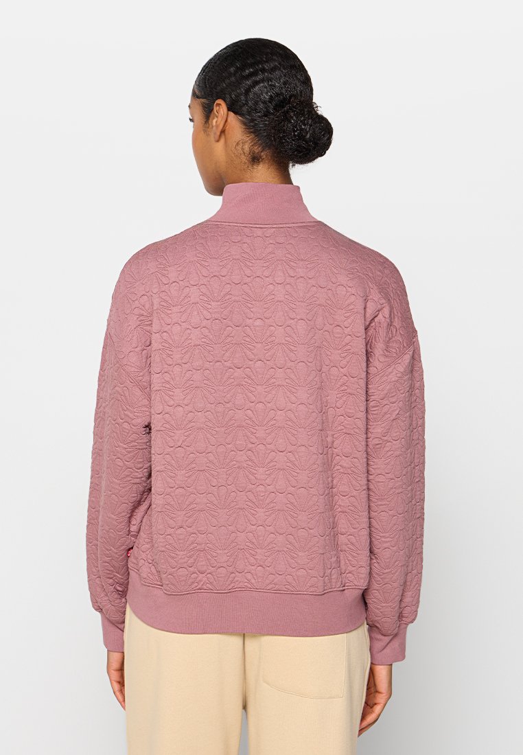 Texturiertes pinkes Sweatshirt mit hohem Kragen und gerippten Abschlüssen. Verfügt über ein durchgängiges Blumenmuster. Die Rückansicht zeigt eine lockere Passform und lange Ärmel.