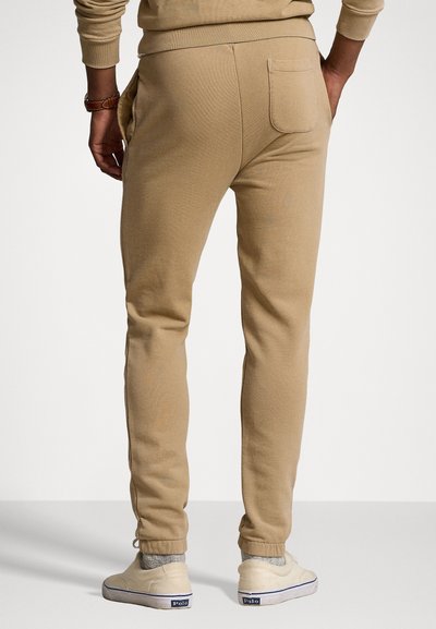 Beige Sweatpants mit schmaler Passform, elastischen Bündchen und einer Gesäßtasche. Hergestellt aus weichem Material und mit einer Kordelzug-Taille für eine verstellbare Passform.