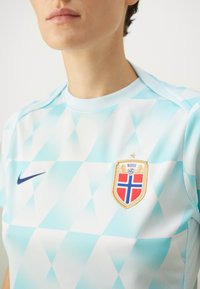 Lyseblå trøye med diamantmønster, Nike-logo i marineblå, og et gyllent våpenskjold med en rød og blå kors og teksten "Norge".